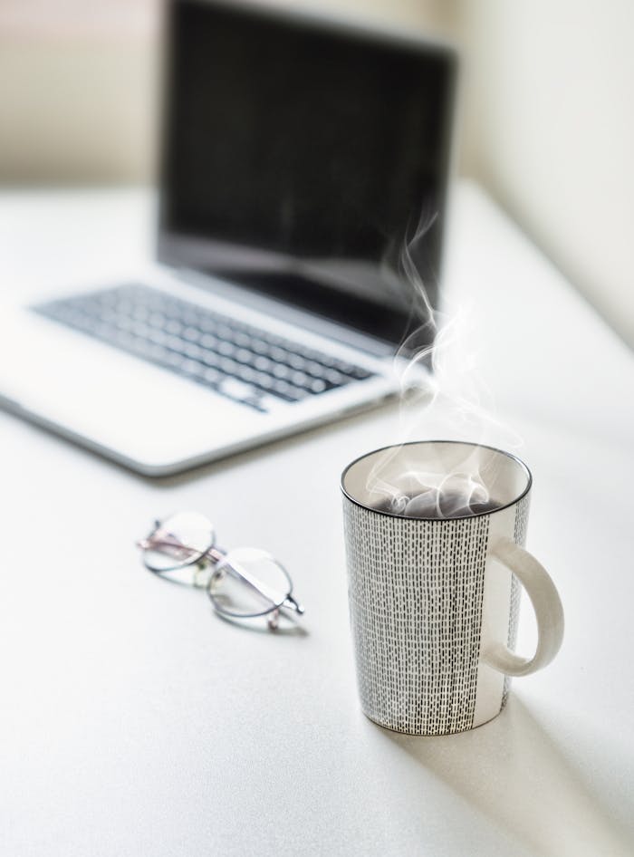 Steaming coffee on a desk next to a laptop and glasses. Perfect for productivity themes.